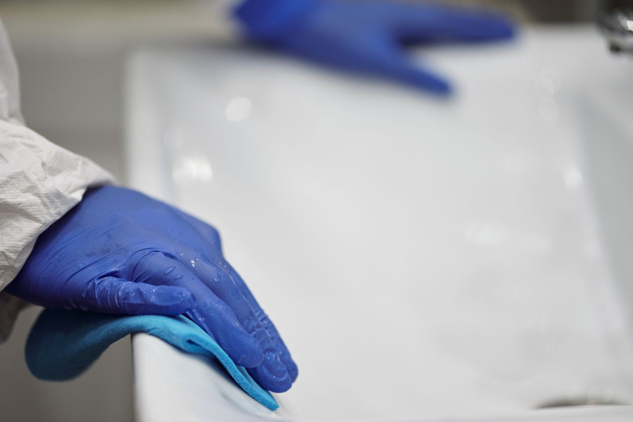 services-06 Close-up of a person sanitizing a bathroom sink with gloves and cloth, focusing on hygiene and cleanliness.