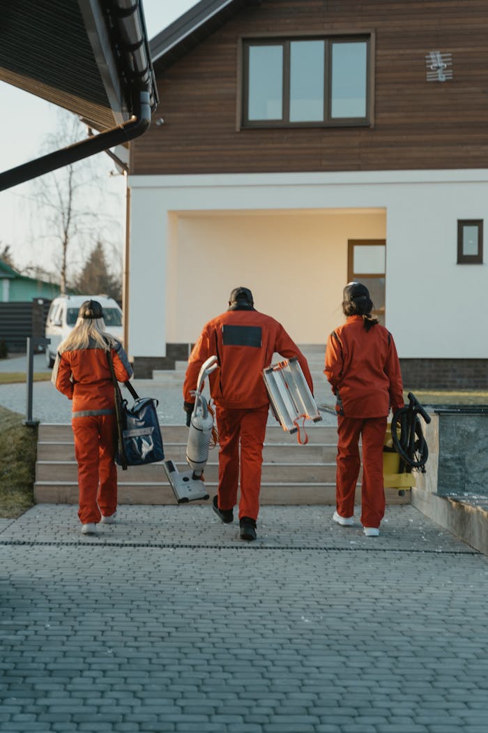 about-us Cleaning crew in red uniforms with equipment approaching a modern house exterior.